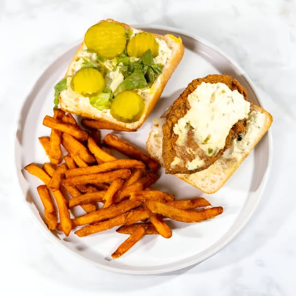 Vegan fried chicken sandwich with creamy sauce, pickles, lettuce, and a side of sweet potato fries.