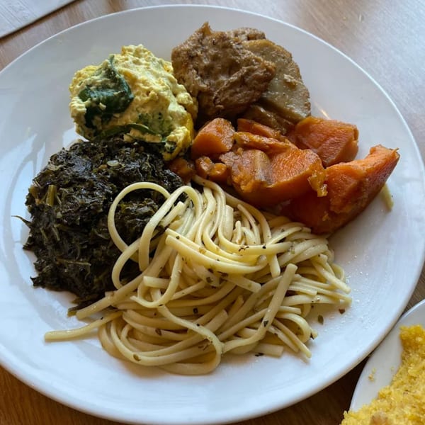 A white plate holds a vegan meal of scrambled tofu, collard greens, sweet potatoes, and pasta.