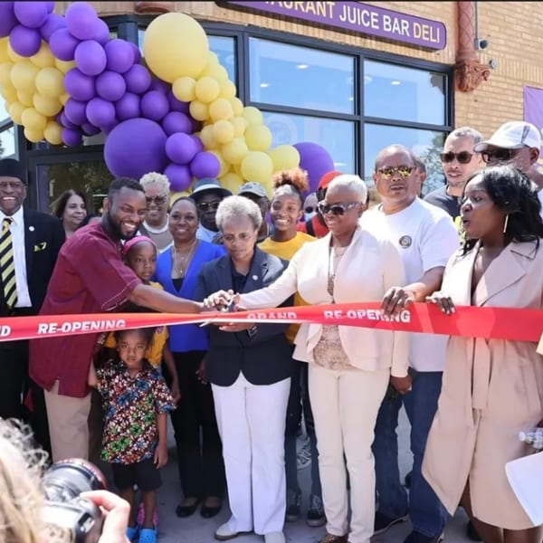 People celebrating the grand re-opening of Soul Veg City, cutting a red ribbon in front of the restaurant.