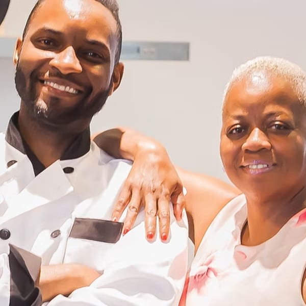 A smiling chef with a beard and an older woman with short hair pose together.