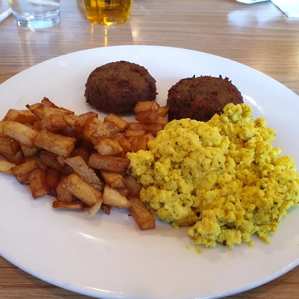 A vegan breakfast plate with two brown patties, golden home fries, and yellow scrambled tofu.