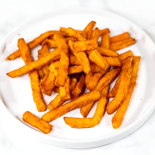 A white plate piled high with golden-brown, crispy sweet potato fries from Soul Veg City.