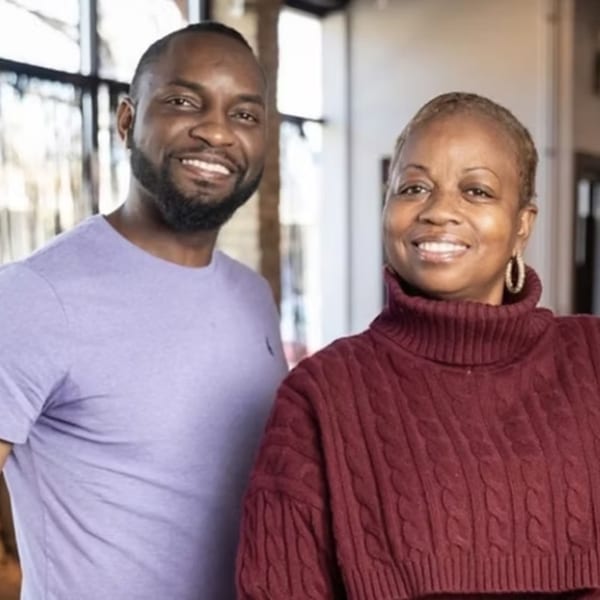 A smiling Black man in a lavender shirt stands next to a smiling Black woman in a red turtleneck.