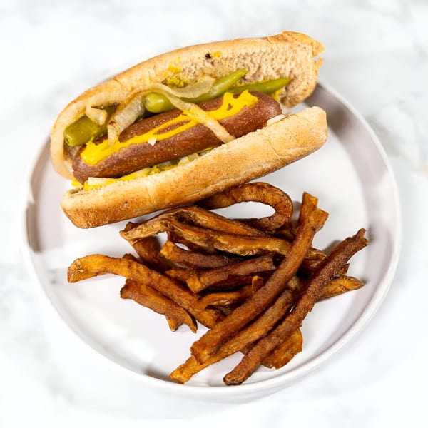 Vegan hot dog with mustard, onions, and relish, served with a side of crispy fries.
