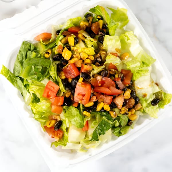 A vibrant vegan salad with fresh lettuce, diced tomatoes, corn, and black beans in a white container.