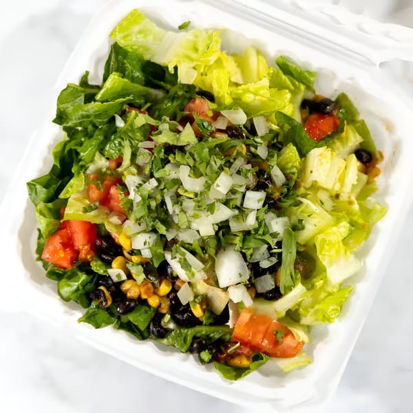 A vibrant vegan salad with lettuce, tomatoes, black beans, corn, and diced onions in a white container.